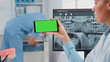© DC Studio - Close up of dentist analyzing smartphone with green screen and teeth scan on computer in dental cabinet. Woman holding device with chroma key for isolated mockup template for dentistry