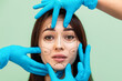 © _KUBE_ - Portrait of a young beautiful woman with surgical markings on her face. Cosmetologists' hands in rubber gloves touch a woman's face. The concept of plastic surgery and cosmetology