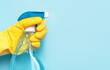 Female hand in glove holds window spray on blue background, spring cleaning concept.