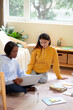© DragonImages - Positive female students sitting on the floor in dormotory room and discussing school project on laptop screen