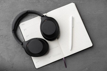 Black headphones on notepad with pen lying on gray background