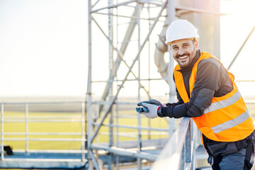 Wall Mural - An industry worker leaning on the railing on the height and smiling at the camera.