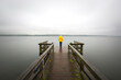 © Westend61 - Germany, Schleswig-Holstein, Woman in yellow jacket standing on edge of lakeshore jetty