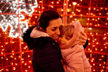 Happy Mother Hugging Daughter In Front Of Christmas Lights
