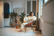 © Westend61 - Happy woman sitting on chair looking out through window at home
