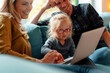 © Westend61 - Smiling father and mother looking at daughter using laptop sitting on sofa at home