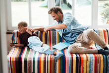 Happy Father Looking At Playful Son Using Smart Phone Sitting On Sofa At Home