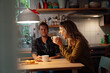 © Westend61 - Cheerful woman holding coffee cup sitting with boyfriend at dining table in kitchen