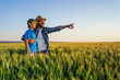 © djoronimo - Father and son are standing in their growing wheat field. Father is teaching his successor about cultivating land.