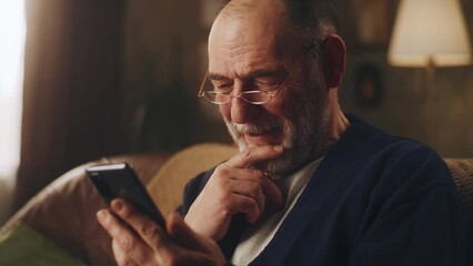 elderly man smiling and watching funny videos on social networks using smartphone and resting in the