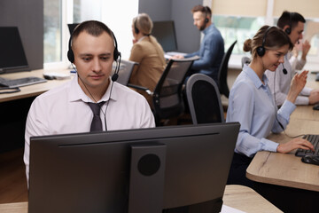 Wall Mural - Call center operators working in modern office, focus on young man with headset