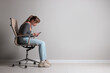 © New Africa - Young woman with poor posture using smartphone while sitting on chair near grey wall, space for text