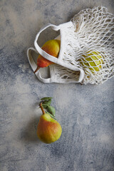 Wall Mural - pears in a knitted white bag on gray with navy cement background, ceramic. place for text.
