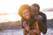 Cheerful black people couple hug and enjoy love and friendship together at the beach with sunset light in background. Concept of young adults relationship in summer holiday vacation outdoor leisure