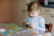 © Irina Schmidt - Excited smiling cute toddler girl playing picture card game. Happy healthy child training memory, thinking. Creative indoors leisure and education of kid. Family activity at home.