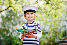 Happy Little Kid Boy In Sailor Capitain Hat And Uniform Playing With Sailor Boat Ship. Smiling Preschool Child Dreaming And Having Fun. Education, Profession, Dream Concept