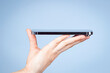 © vejaa - Woman hand holding smartphone screen face up side view on light blue background