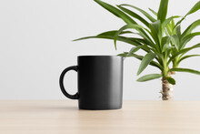 Black Mug Mockup On The Wooden Table With A Yucca Plant.