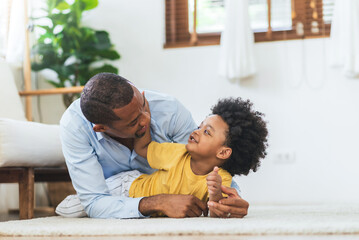 Happy African American Father and little child son playing on the floor at home together, Black family concept.