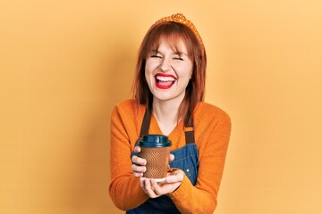 Sticker - Redhead young woman wearing waitress apron holding take away cup of coffee smiling and laughing hard out loud because funny crazy joke.