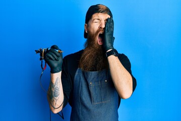 Wall Mural - Redhead man with long beard tattoo artist wearing professional uniform and gloves yawning tired covering half face, eye and mouth with hand. face hurts in pain.