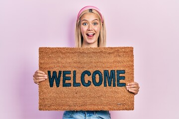 Poster - Beautiful blonde woman holding welcome doormat celebrating crazy and amazed for success with open eyes screaming excited.