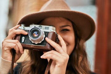 Wall Mural - Young hispanic tourist woman smiling happy using vintage camera at the city.