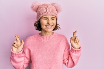 Canvas Print - Young brunette woman wearing cute wool cap gesturing finger crossed smiling with hope and eyes closed. luck and superstitious concept.