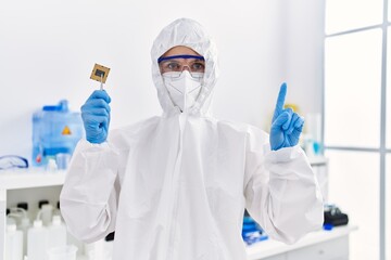 Sticker - Young blonde woman holding cpu computer processor at laboratory surprised with an idea or question pointing finger with happy face, number one