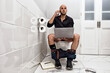 © Scopio - Mature man working online while using the bathroom
