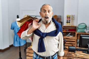 Poster - Handsome senior man holding shopping bags at boutique shop scared and amazed with open mouth for surprise, disbelief face