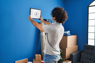 Sticker - Young hispanic man hanging photo on wall at new home