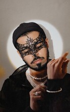 Portrait Of South Asian Man With Lace Masquerade And Pearl Necklace Against Light Background