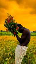 Side View Of Topless Man Holding Red Flowers Standing On Grass Field