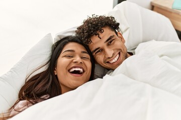 Canvas Print - Young latin couple covering with bedsheet lying on the bed at bedroom.