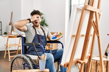 Sticker - Young hispanic man sitting on wheelchair painting at art studio peeking in shock covering face and eyes with hand, looking through fingers with embarrassed expression.