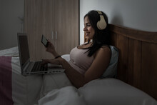 Woman Using Laptop And Headphones In Bed