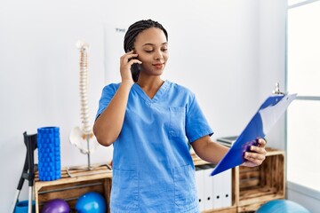 Canvas Print - Young african american woman wearing physio therapist uniform talking on the smartphone at clinic