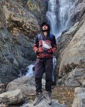 Young South Asian Man With Backpack Standing On Brown Rock Near Waterfalls