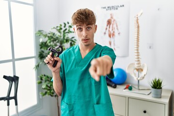 Sticker - Young caucasian physio man holding hand grip to train muscle at the clinic pointing with finger to the camera and to you, confident gesture looking serious