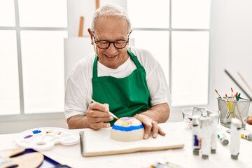 Sticker - Senior grey-haired artist man smiling happy painting pottery sitting on the table at art studio.