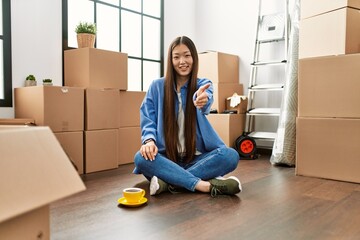 Canvas Print - Young chinese girl sitting on the floor at new home smiling friendly offering handshake as greeting and welcoming. successful business.