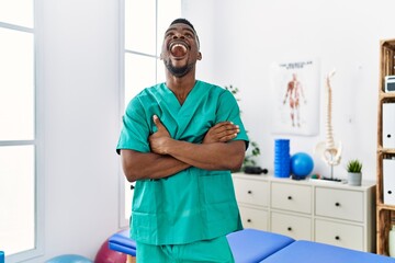 Sticker - Young african physiotherapist man with crossed arms working at pain recovery clinic angry and mad screaming frustrated and furious, shouting with anger looking up.