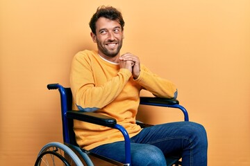 Poster - Handsome man with beard sitting on wheelchair laughing nervous and excited with hands on chin looking to the side