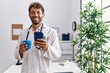 © Krakenimages.com - Young hispanic man wearing doctor uniform using smartphone and drinking coffee at clinic