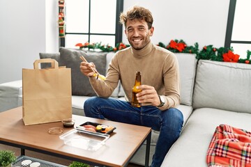 Young hispanic man eating take away sushi sitting by christmas decor at home