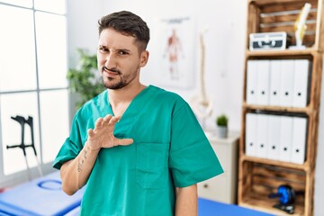 Sticker - Young physiotherapist man working at pain recovery clinic disgusted expression, displeased and fearful doing disgust face because aversion reaction.