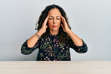 Poster - Beautiful middle age woman wearing casual clothes sitting on the table with hand on head for pain in head because stress. suffering migraine.