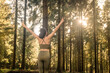 © Rob Wilkinson - Woman stretching arms and breathing fresh air in middle of a forest while exercising at sunrise.