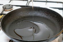 The process of pouring vegetable oil into a cast iron heated frying pan.
